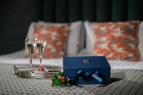 navy gift box with christmas holly and a tray of two glasses of prosecco sitting on a bed at clandeboye lodge