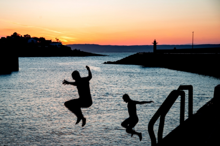 Two people jumping into the sea at sunset in Bangor, Northern Ireland.